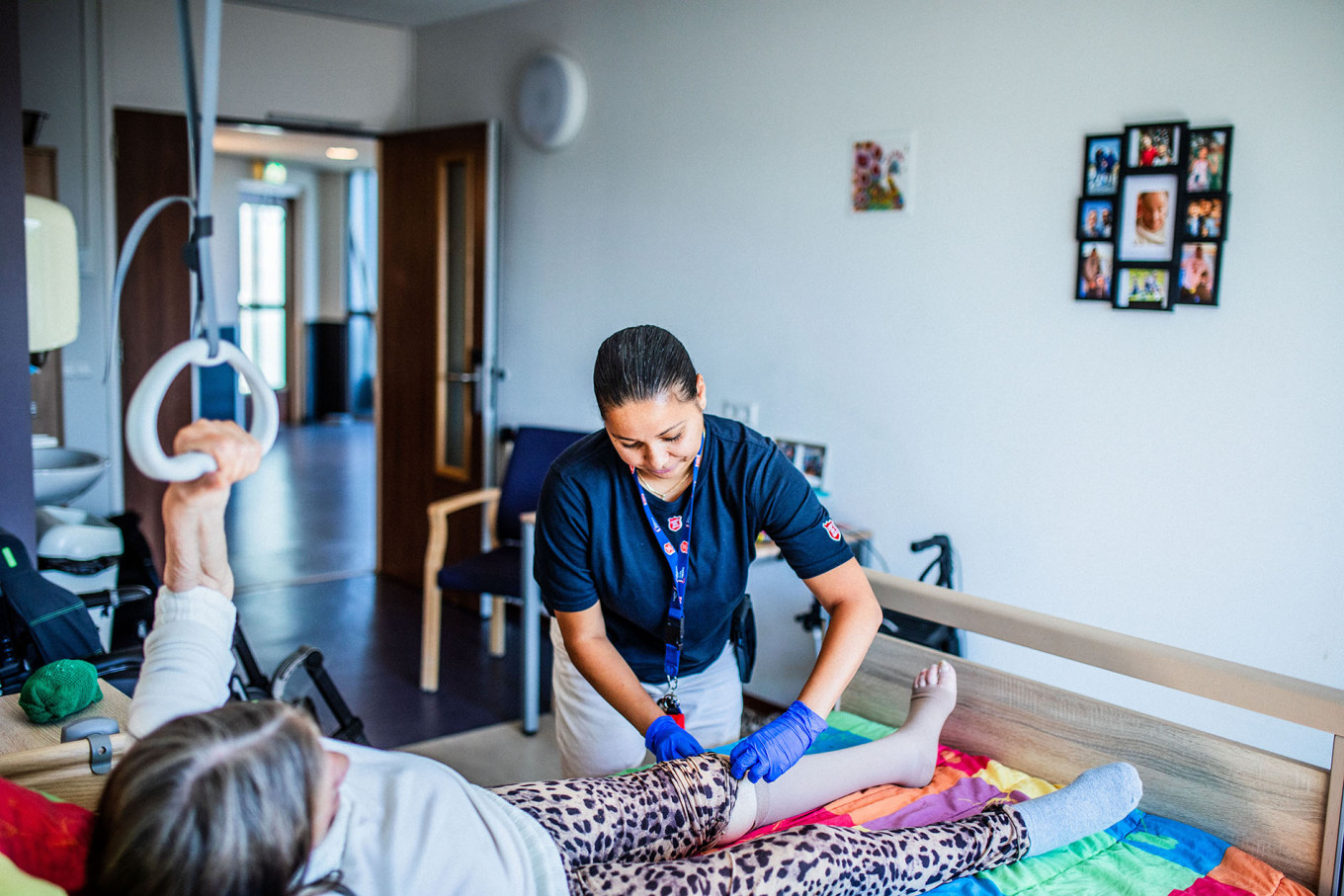 Vrouw ligt op bed, Leger des Heils verpleegkundige verbindt haar knie  