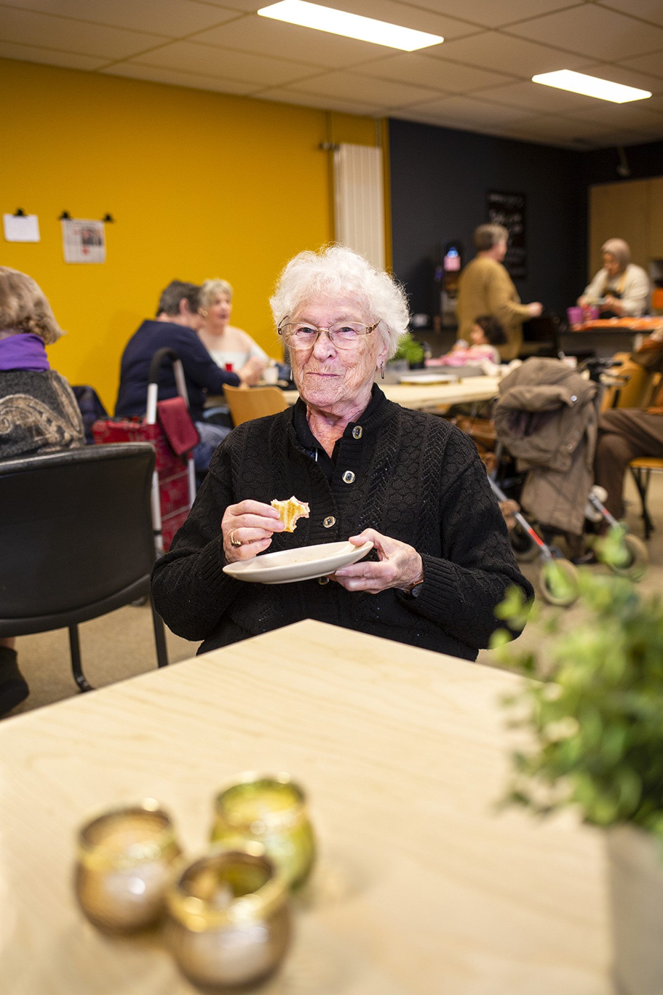 vrouw met wit, krullend haar en bril eet cake Buurthuiskamer Schiedam Erik Buis