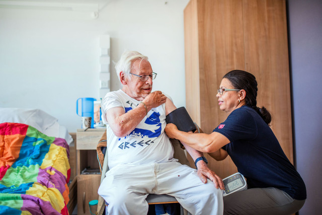 Verpleegkundige van Leger des Heils doet bloeddruk-band om arm van man in rolstoel